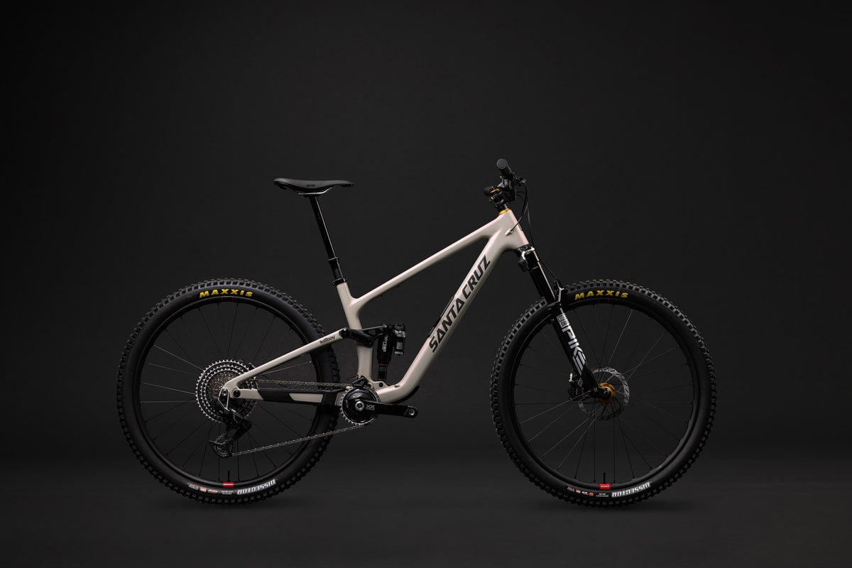 Santa Cruz full-suspension mountain bike in a light beige frame with black components, shown in profile against a dark studio background.